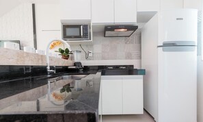 A modern kitchen with white cabinets, a black countertop, a built-in microwave, and a white refrigerator. - Apt 400m From the Beach of Taperapua/ BA Edt0011 (Porto Seguro)