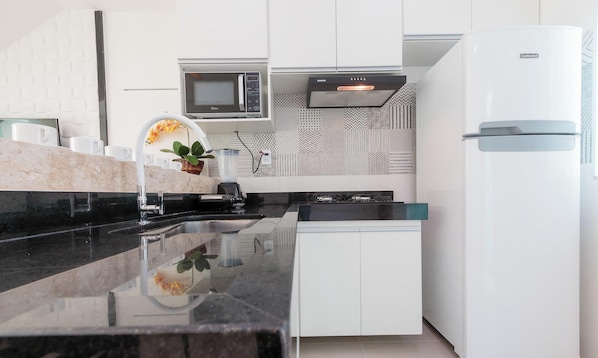 A modern kitchen with white cabinets, a black countertop, a microwave, a stove, and a refrigerator. - Apt 400m From the Beach of Taperapua/ BA Edt0011 (Porto Seguro)
