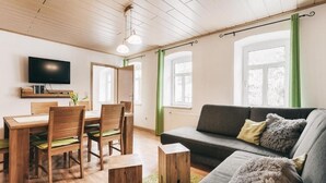 A modern living room with a wooden dining table, chairs, a grey sofa, and a flat-screen TV mounted on the wall. - Super apartment for up to 6 people in Königstein, right next to the fortress. (Königstein)