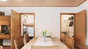 A dining area with a wooden table and chairs, a vase with flowers, and wooden cabinets. - Super apartment for up to 6 people in Königstein, right next to the fortress. (Königstein)