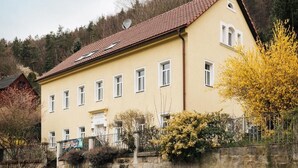 A yellow building with a red-tiled roof, multiple windows, and a stone wall in front. - Super apartment for up to 6 people in Königstein, right next to the fortress. (Königstein)