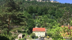 A hillside with a building featuring a red roof and multiple windows. - Super apartment for up to 6 people in Königstein, right next to the fortress. (Königstein)