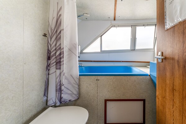 Une petite salle de bain comprenant des toilettes, un rideau de douche, une fenêtre et un lavabo bleu.