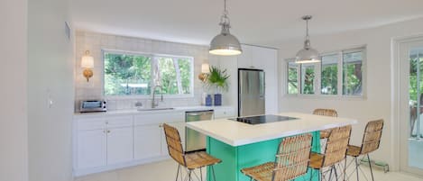 A modern kitchen with white cabinets, a central island with bar stools, and pendant lighting.