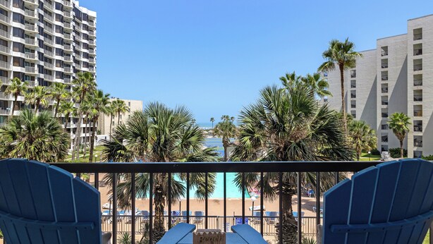 A balcony with two chairs, a table, and a view of a beach and hotel buildings. - Steps to Pool & Beach: South Padre Island Retreat! (South Padre Island)