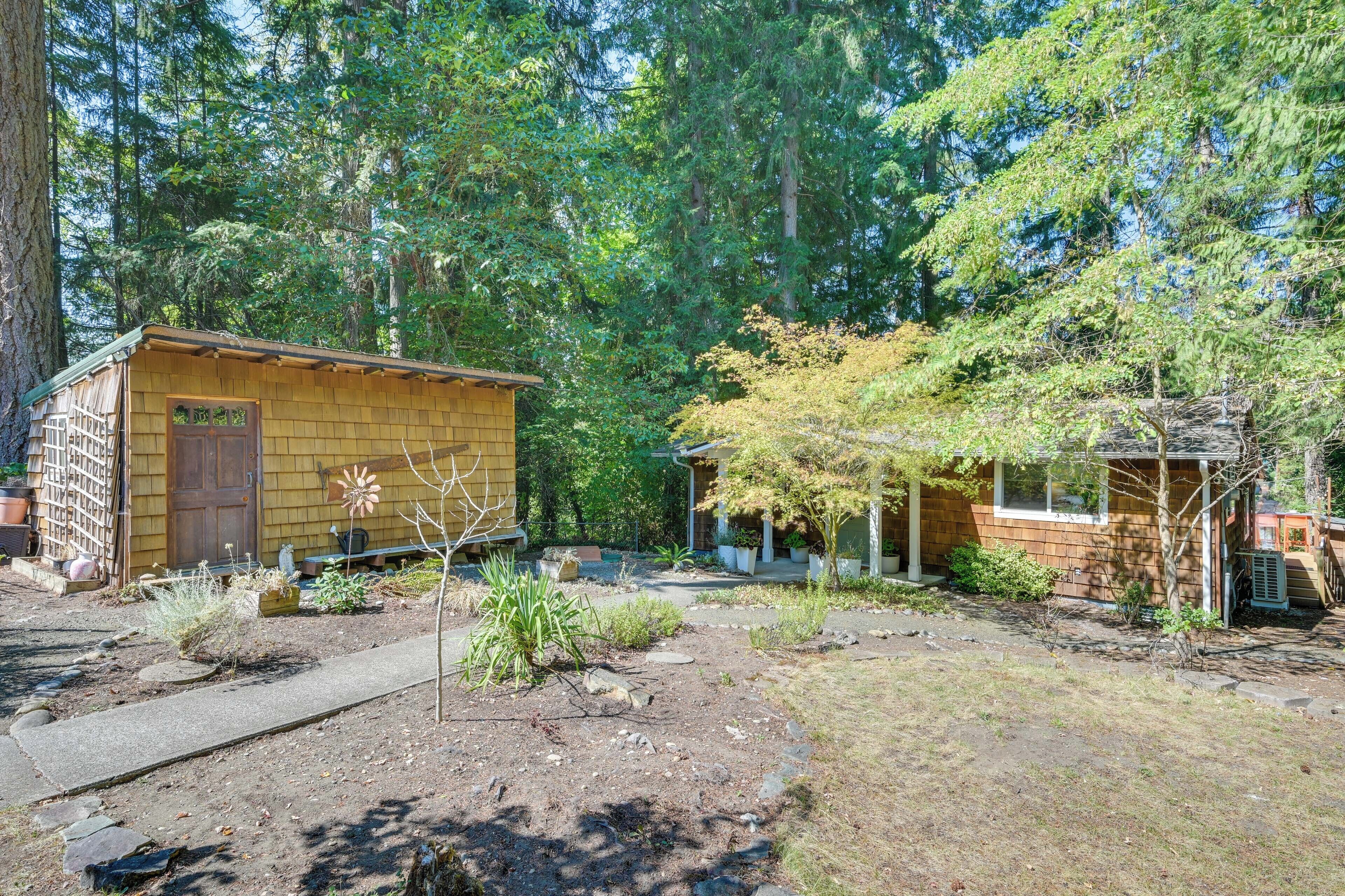 A rustic cabin with a wooden exterior, surrounded by a garden with various plants and a paved pathway.