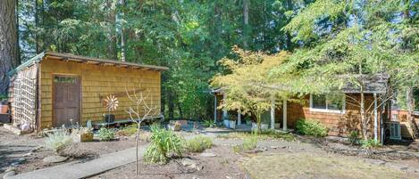 A rustic cabin with a wooden exterior, surrounded by a garden with various plants and a paved pathway.