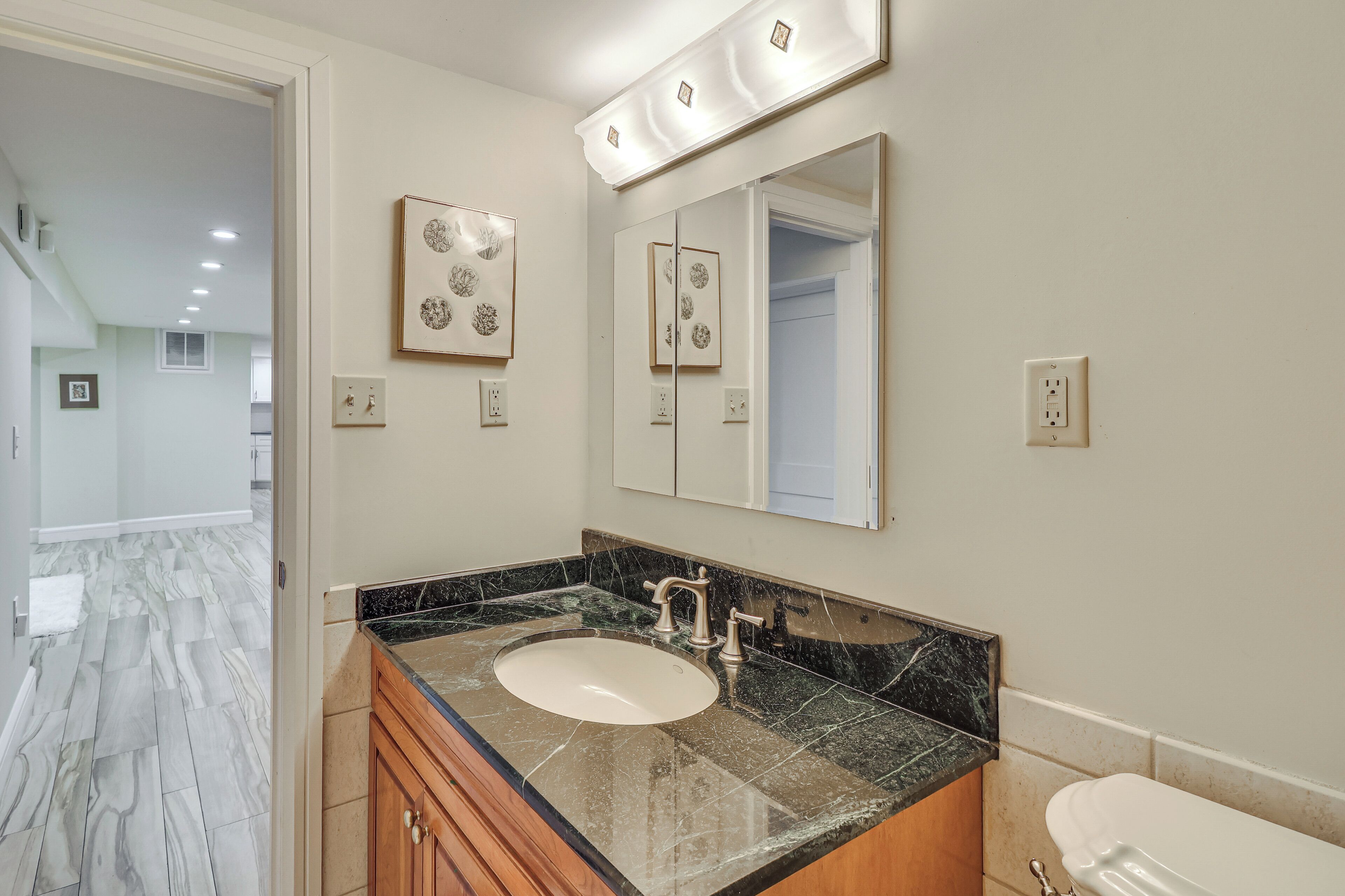 A bathroom with a marble sink, wooden cabinets, a large mirror, and a toilet.