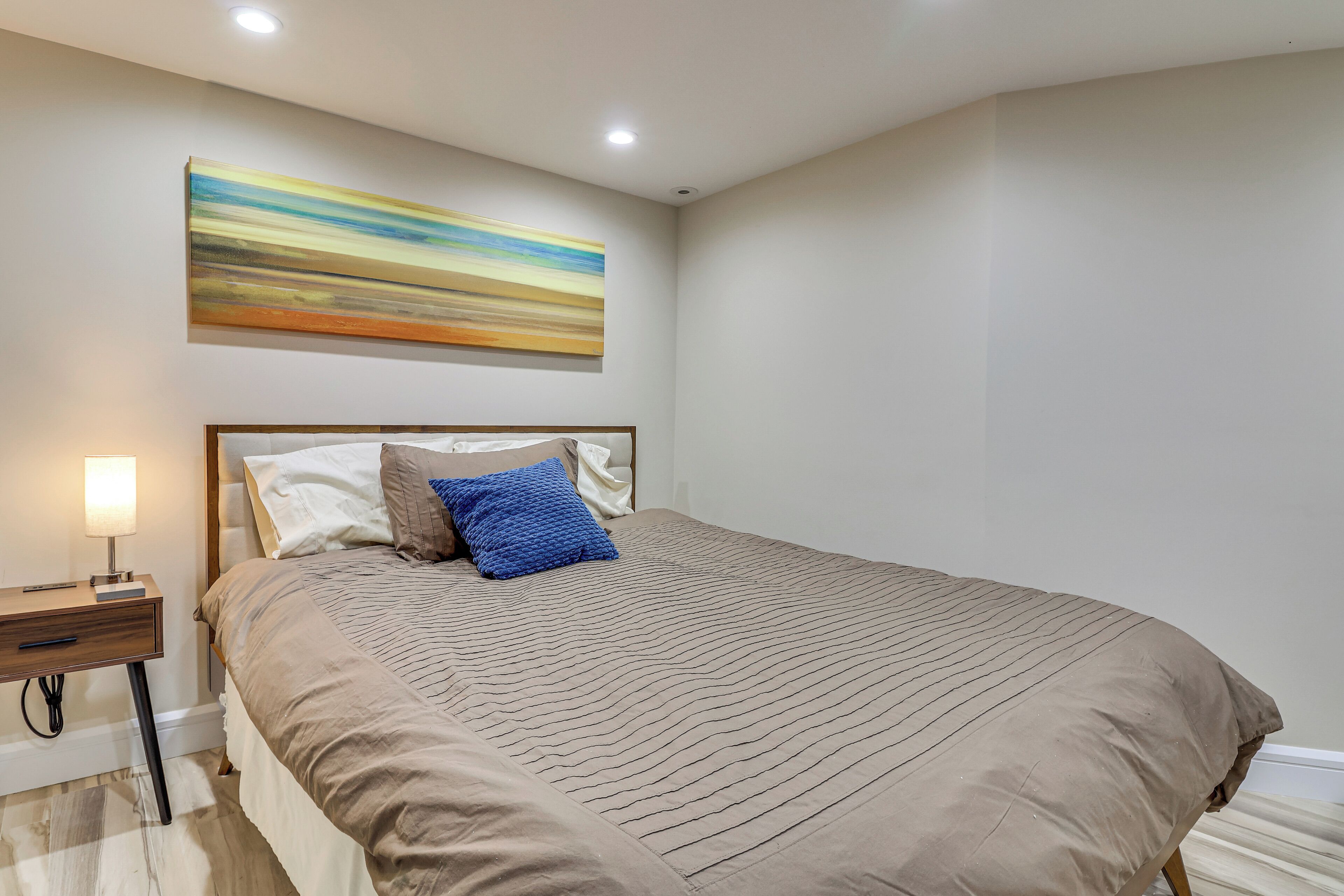 Een slaapkamer met een groot bed, een nachtkastje met een lamp en een schilderij aan de muur.