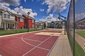 Een basketbalveld met een hek van gaas, omringd door huizen, met een heldere lucht erboven.