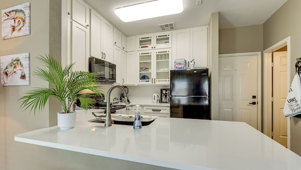 A modern kitchen with white cabinetry, a stainless steel refrigerator, and a central island with a sink. - Poolside Bliss & Lake Fun: Monkey Island Retreat! (Afton)