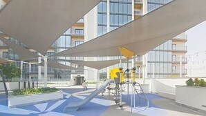 Area giochi all'aperto con scivoli e strutture per arrampicata, circondata da edifici moderni.