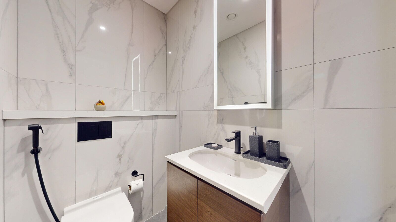 Un baño moderno con suelo de mármol, un lavabo blanco, un espejo y un inodoro.