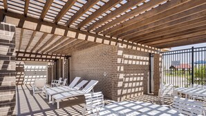 An outdoor patio area with brick walls, wooden pergola, and white furniture. - Spacious Family Home w/ Office in Midland-odessa! (Midland)