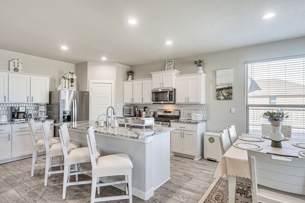 A modern kitchen with white cabinetry, a central island, and a dining area with a table and chairs. - Spacious Family Home w/ Office in Midland-odessa! (Midland)