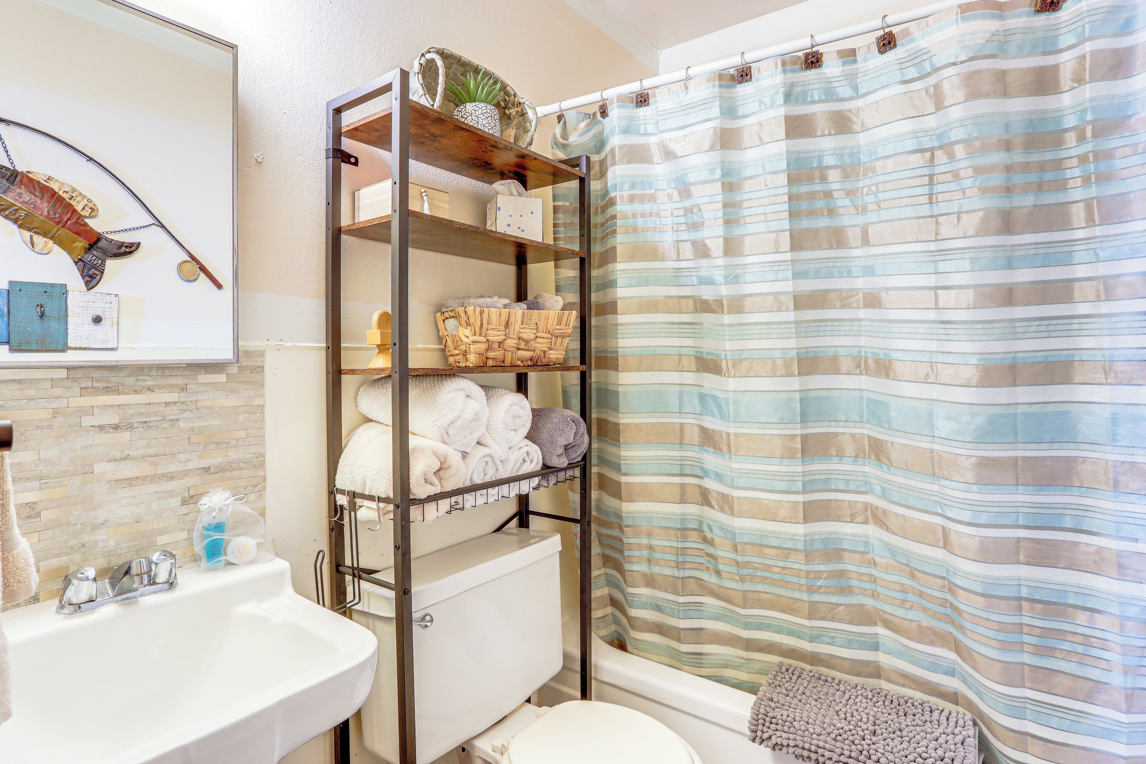 A bathroom with a shower curtain, a sink, a toilet, and a shelf with towels and baskets.