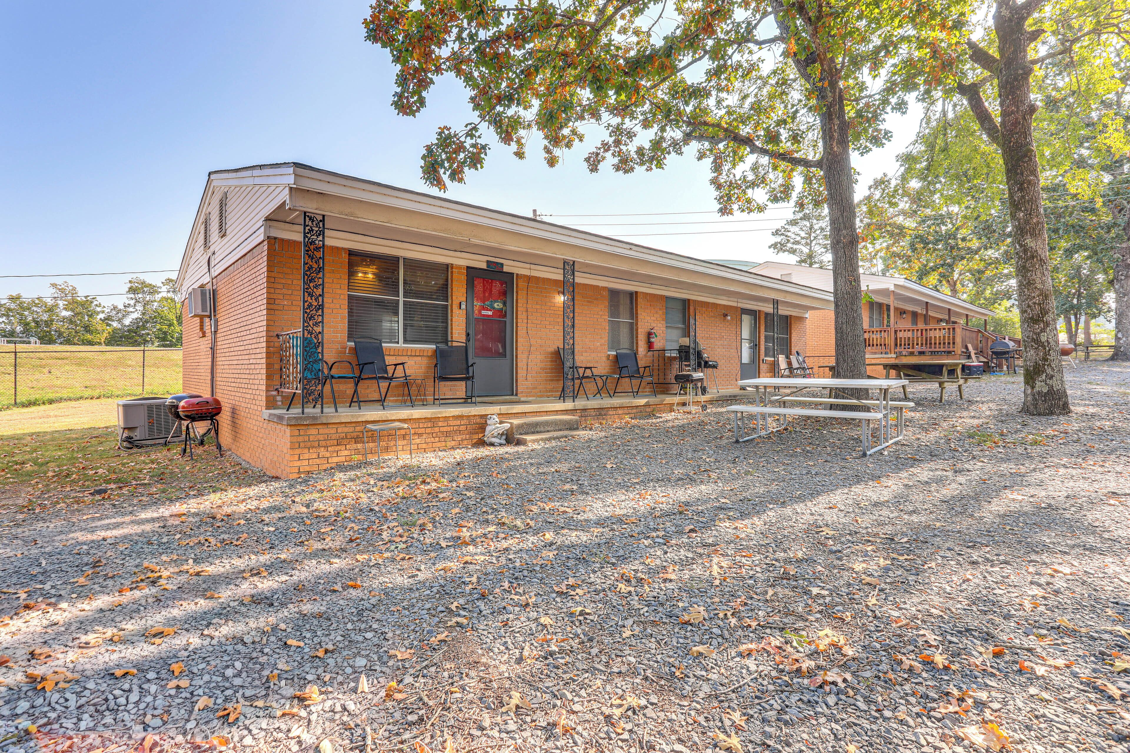 A motel with a covered outdoor seating area, a barbecue grill, and a gravel driveway.