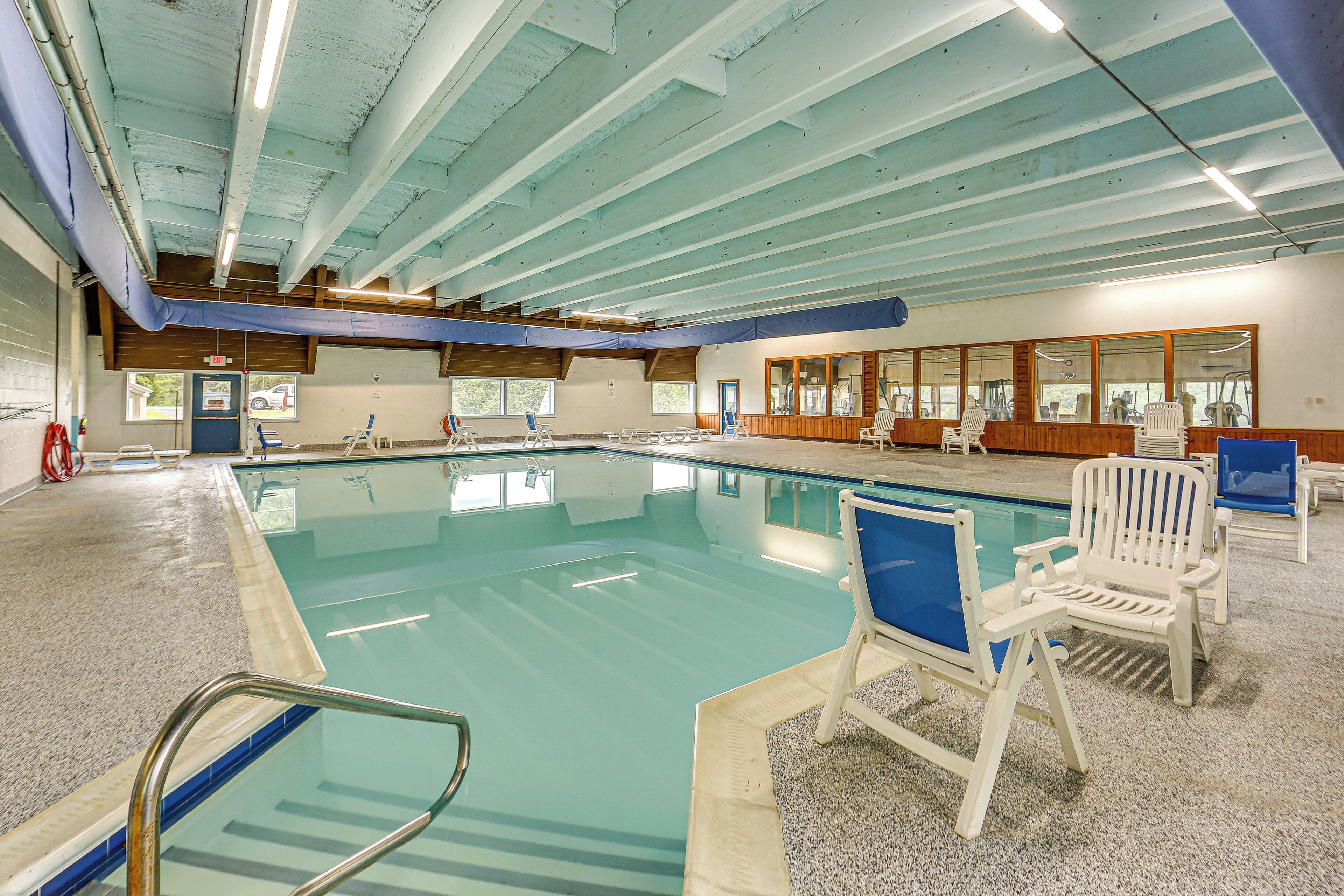 An indoor swimming pool with clear water, surrounded by white lounge chairs and a tiled floor.