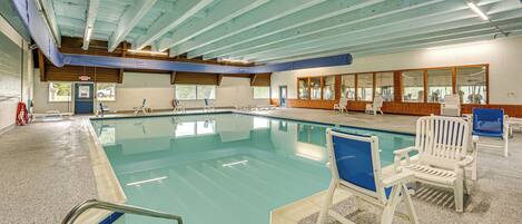 An indoor swimming pool with clear water, surrounded by white lounge chairs and a tiled floor.