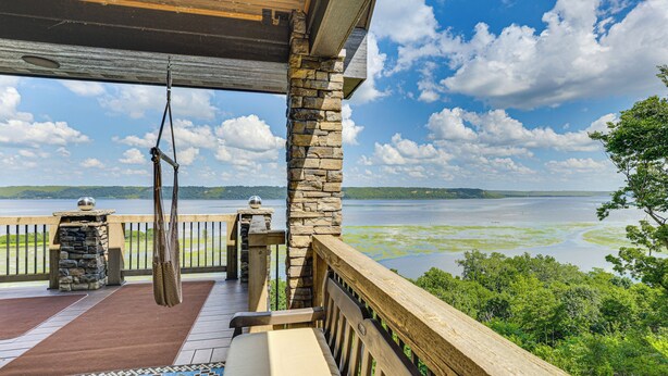 A wooden deck with a stone pillar, a swing, and a view of a lake. - River Views + Wraparound Deck: Dubuque Getaway (Dubuque)