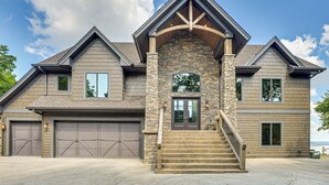A two-story house with a stone facade, a central entrance with a staircase, and two garage doors. - River Views + Wraparound Deck: Dubuque Getaway (Dubuque)