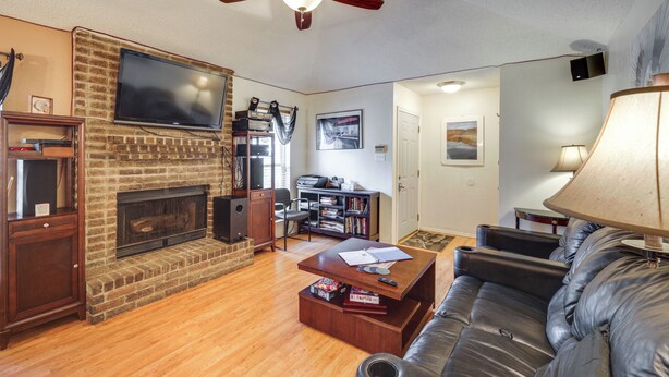 A living room with a brick fireplace, a flat-screen TV mounted above it, a ceiling fan, and a leather sofa.