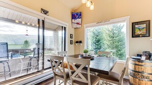 A dining area with a large table, wooden chairs, and a view of a snowy landscape through a glass door.