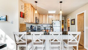 A kitchen with wooden cabinets, a refrigerator, and a bar area with white chairs.
