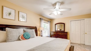 A bedroom with a bed, a ceiling fan, a dresser, a mirror, and a door.