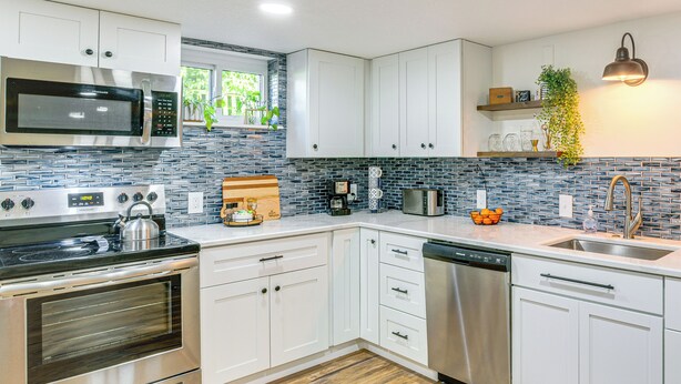 A modern kitchen with white cabinets, stainless steel appliances, and a blue-tiled backsplash. - 6 Mi to Cpkc Stadium: Convenient Kansas City Apt (Riverside)