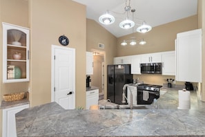 A modern kitchen with white cabinets, a stainless steel refrigerator, a microwave, and a gas stove.