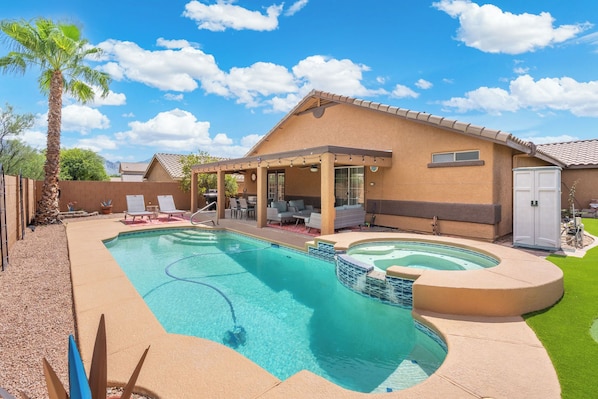 A backyard with a swimming pool, patio furniture, and a covered seating area.