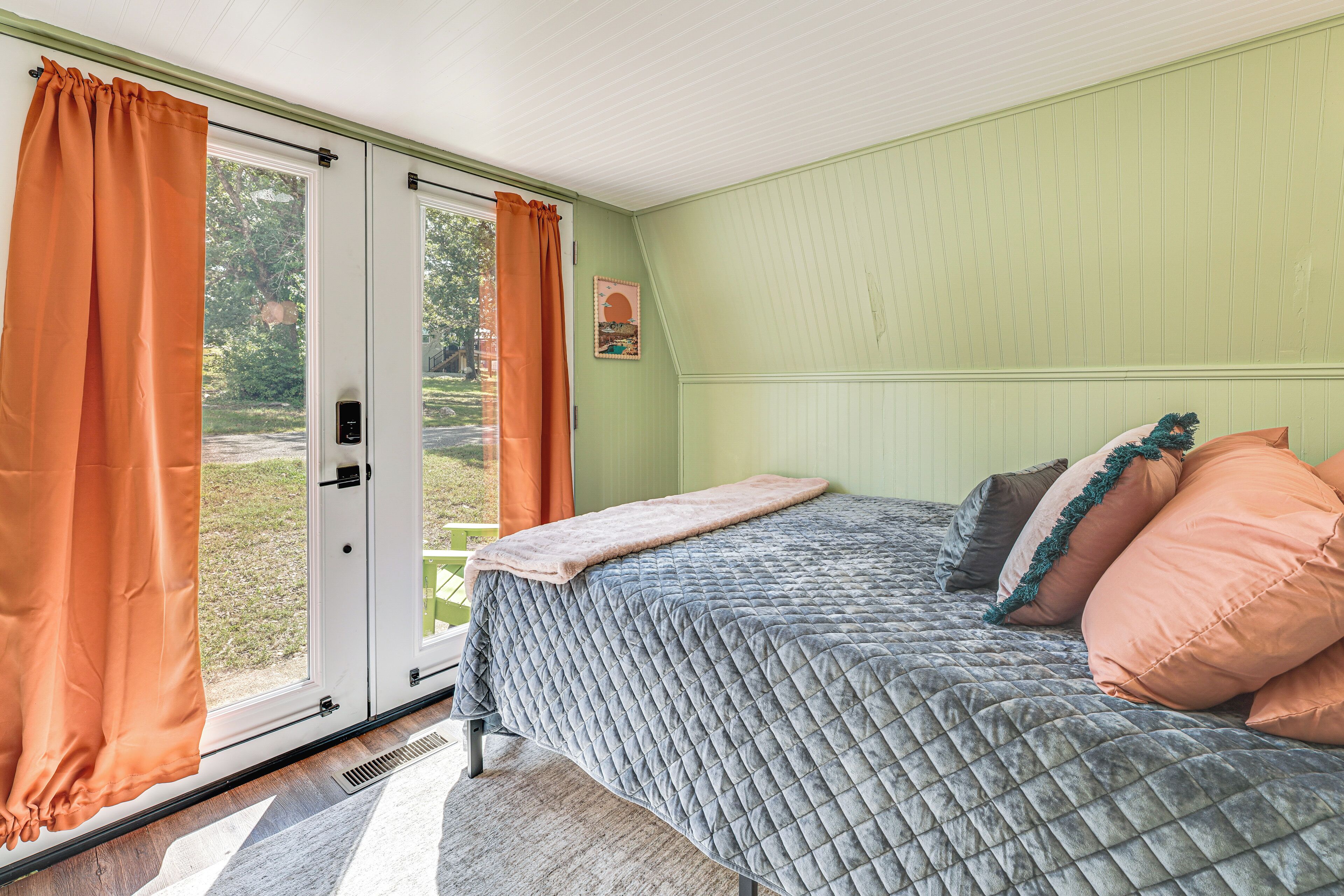 Une chambre à coucher avec un lit, des rideaux orange, une fenêtre et une porte.