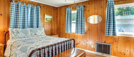 A bedroom with a wooden bed, a nightstand, a dresser, a ceiling fan, and a window with plaid curtains.