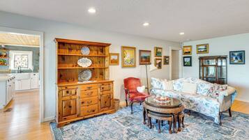 A living room with a wooden cabinet, a red chair, a patterned sofa, and a dining table with chairs.