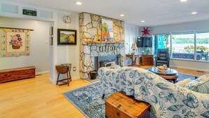 A living room with a stone fireplace, a sofa, a coffee table, and a view of the outdoors. - Across Water From Belfair SP: Hood Canal Cottage! (Belfair)