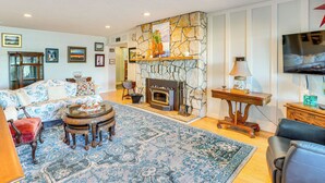 A living room with a stone fireplace, a large TV, and a patterned rug. - Across Water From Belfair SP: Hood Canal Cottage! (Belfair)