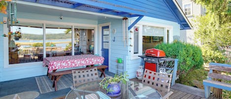Et blåt hus med en terrasse, et bord med stole og en grill.