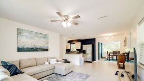 A modern living room with a sofa, a coffee table, a ceiling fan, and a kitchen area in the background. - Tree-lined Retreat 4 Mi to Three Sisters Springs! (Crystal River)