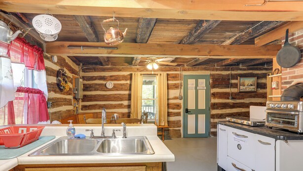 A rustic cabin-style kitchen with wooden walls, a sink, a stove, and a ceiling fan. - 5 Mi to State Parks: Penfield Cabin w/ Fire Pit! (Penfield)