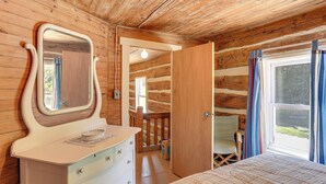 A wooden cabin room with a bed, a dresser, a mirror, and a window with curtains. - 5 Mi to State Parks: Penfield Cabin w/ Fire Pit! (Penfield)