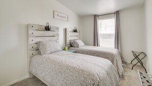 Une chambre avec deux lits, une petite table, une chaise, une fenêtre avec des rideaux et un luminaire fixé au mur.