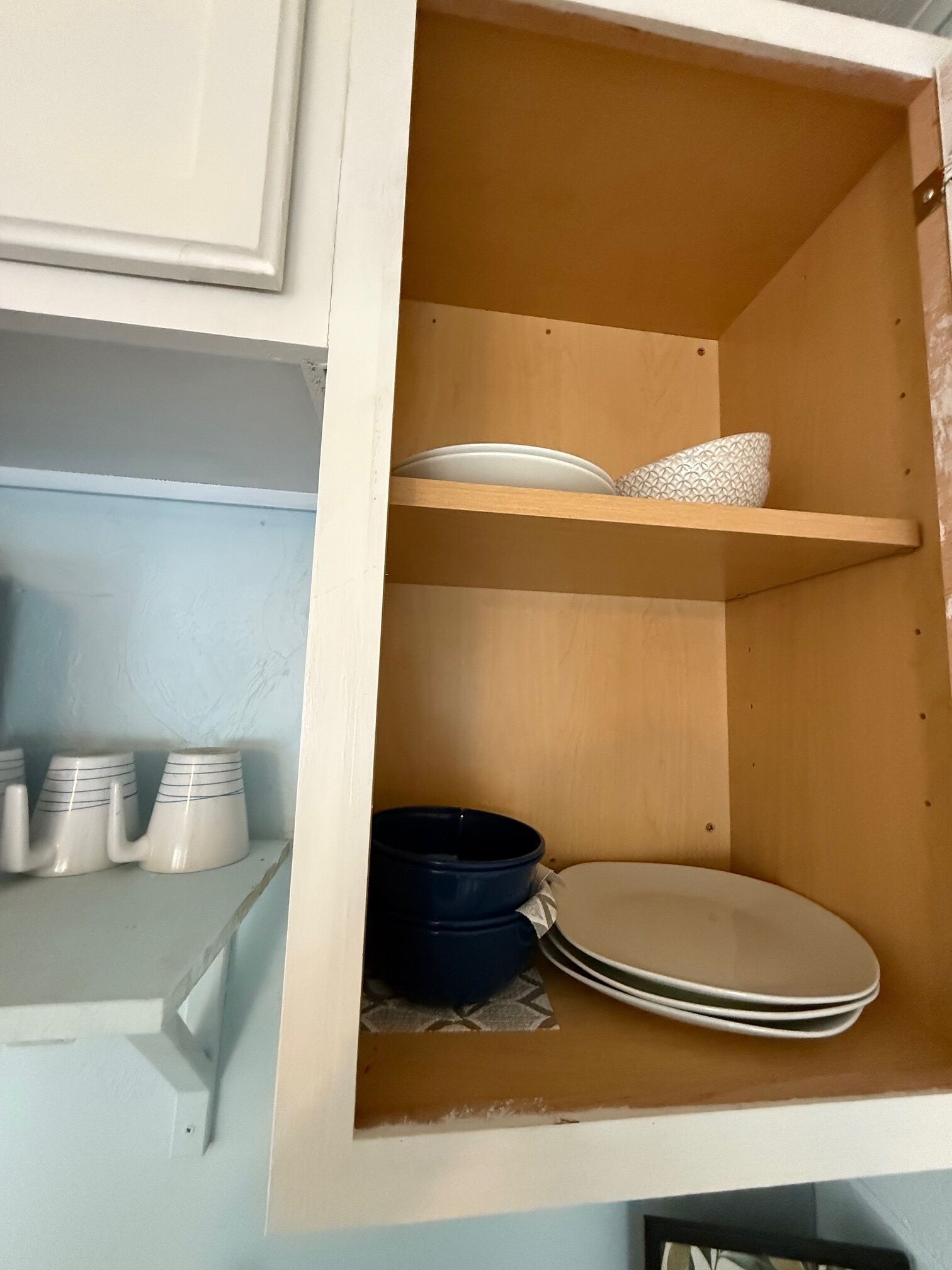 A kitchen cabinet with shelves holding plates, bowls, and mugs.