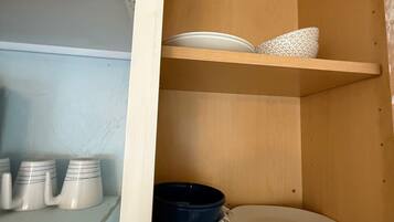 A kitchen cabinet with shelves holding plates, bowls, and mugs.