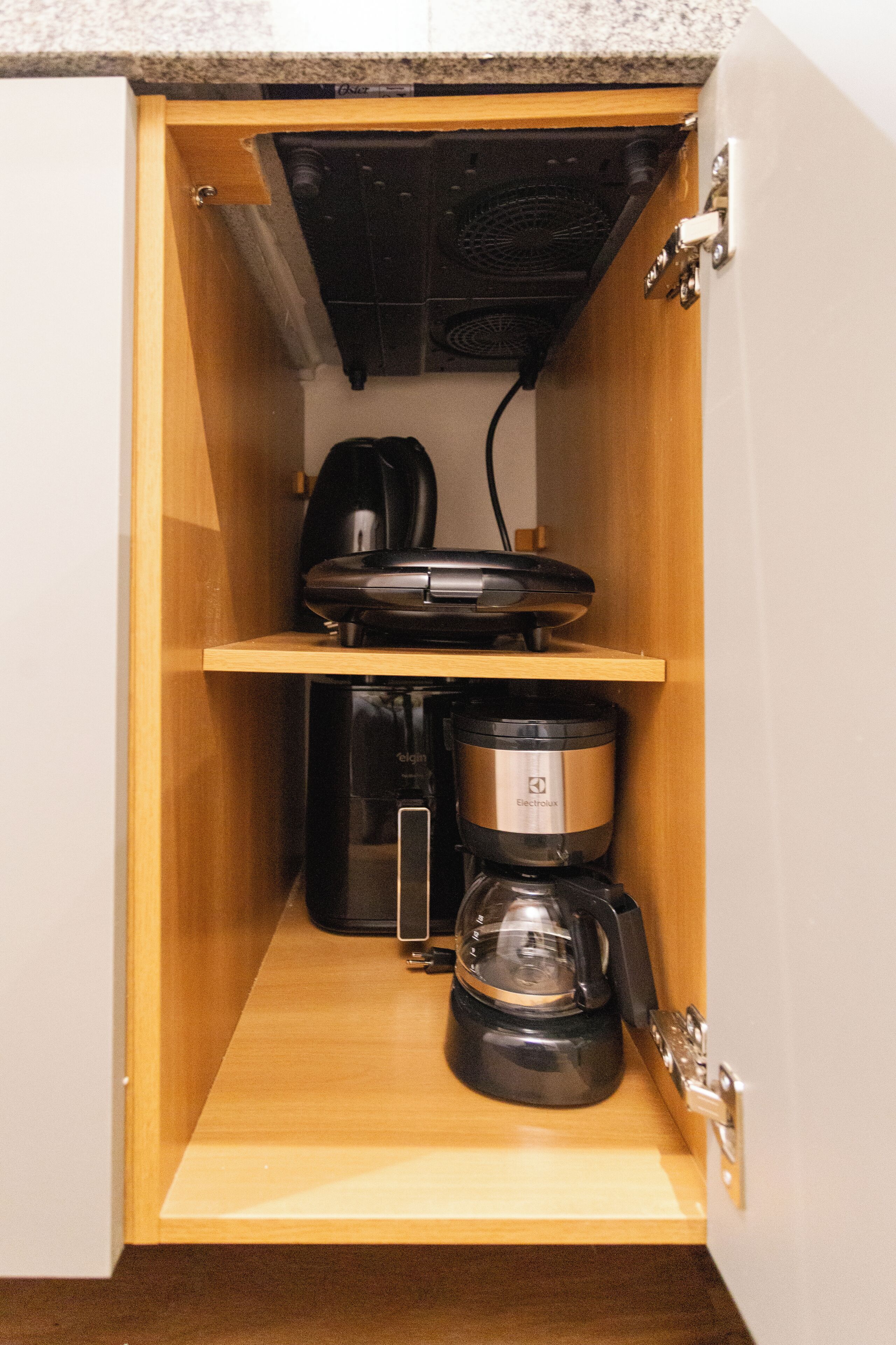 A kitchen cabinet with a coffee maker and a kettle.