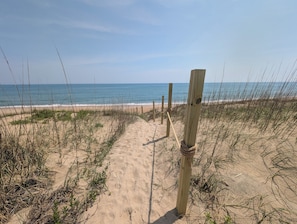 A sandy beach path leading to the ocean, with wooden posts and ropes for guidance.