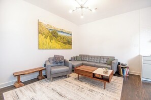 A living room with a grey sectional sofa, a wooden coffee table, a bench, and a painting on the wall. - Fells Point Charm with a View (Baltimore)