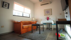 Een woonkamer met een bank, een salontafel, een eettafel met stoelen en een aan de muur bevestigde televisie.