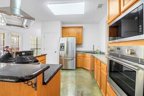 A modern kitchen with stainless steel appliances, wooden cabinets, and a black countertop. - Charming Kyle Retreat with Pool, Porch & Walk to Downtown (Kyle)