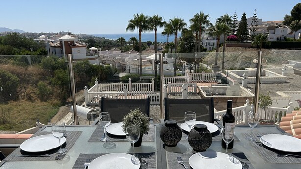 Mesa de comedor para cuatro con vista al mar y colinas al fondo.